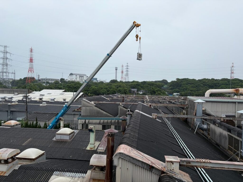 クレーンで屋上へ業務用エアコンを吊り上げる搬入作業