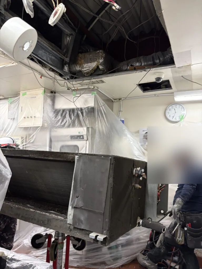 天井を開口して厨房から業務用エアコン本体を降ろしている作業員