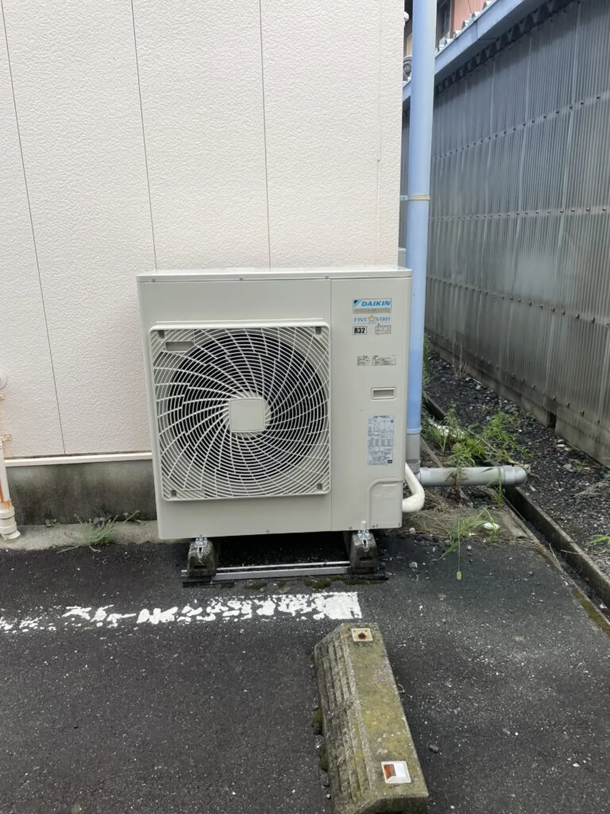 建物の外壁沿いの地面に設置された室外機と周りの草